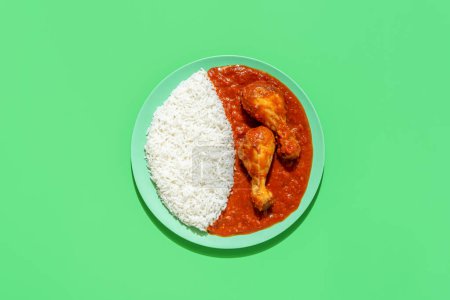 Foto de Delicious tomato chicken stew and rice as a side dish, minimalist on a green table. Above view with a plate with rice and chicken legs in tomato sauce. - Imagen libre de derechos