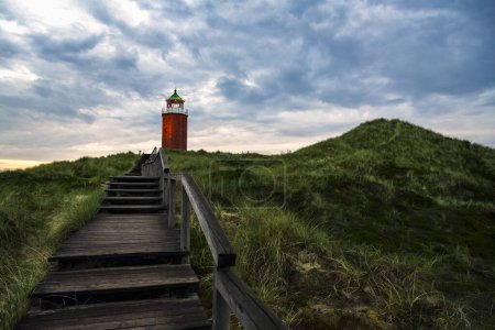 Foto de Paisaje nocturno con escaleras de madera sobre la colina de hierba de marram, hacia el faro rojo, en la isla de Sylt, Alemania - Imagen libre de derechos