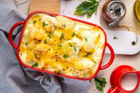 Loaded cheesy vegetable cauliflower casserole, with creamy sauce, baked autumn vegan dish, on light tiled background copy space