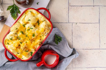 Loaded cheesy vegetable cauliflower casserole, with creamy sauce, baked autumn vegan dish, on light tiled background copy space