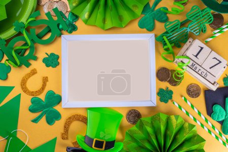 Photo for Happy Patrick's Day greeting card, party invitation. Accessories for St Patrick holiday leprechaun hat, glasses, shamrock, gold coins, block calendar March 17 date, ornaments, gold background top view - Royalty Free Image