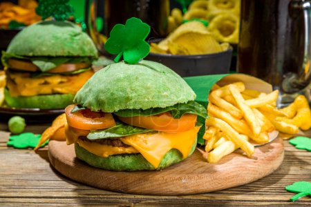 Photo for St Patrick`s holiday party invitation, bar menu background. Irish St Patrick`s day beer, ale glasses, snacks, appetizer, green burger, wooden bar table with shamrock, clover, coins, leprechaun hat - Royalty Free Image