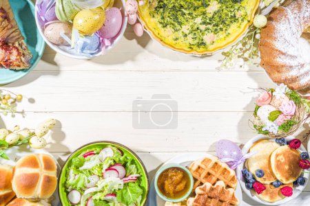 Cena festiva, almuerzo de Pascua. Platos tradicionales de Pascua en la mesa de la casa de la familia carne al horno, quiche, ensalada de primavera, magdalena, huevos de colores, bollos de cruz caliente