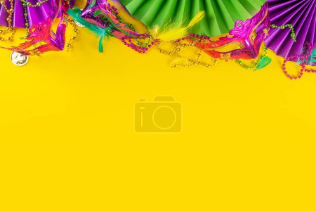 Photo for Mardi Gras colorful holiday greeting card background with festival masquerade accessories, decor, carnival mask, beads, feathers, fan on bright background traditional yellow purple green colors - Royalty Free Image