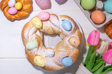 Easter wreath bread, traditional Easter holiday baking, sweet bun cakes with colorful Easter eggs, on brunch holiday decorated table copy space