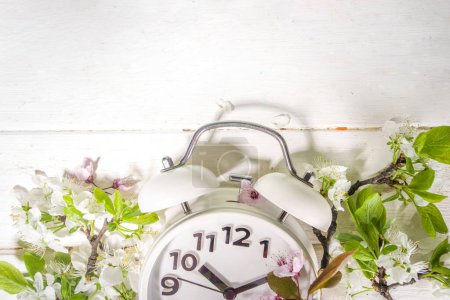 Foto de Spring Forward Time, Concepto de ahorro de luz diurna con reloj despertador y jardín de primavera Flores sobre fondo de madera espacio de copia plana sobre fondo blanco de madera - Imagen libre de derechos