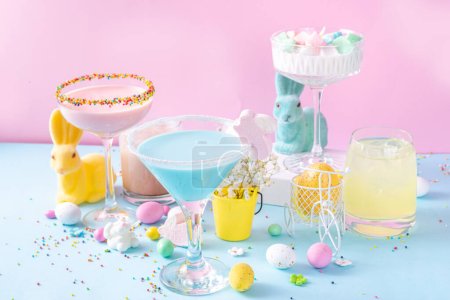 Colorful pastel colored kids Easter party mocktails, Creamy and iced non-alcohol drinks with cotton candy, marshmallow, sugar sprinkles and Easter eggs, on blue pink pastel background copy space
