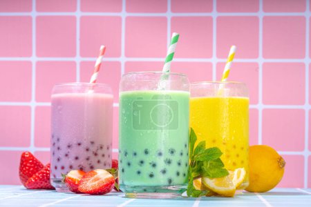 Set of three colorful summer bubble tea, bright creamy pearl tea or latte tapioca drinks, pink berry, yellow citrus, green mint, with tapioca balls and crushed ice, on colorful tile background