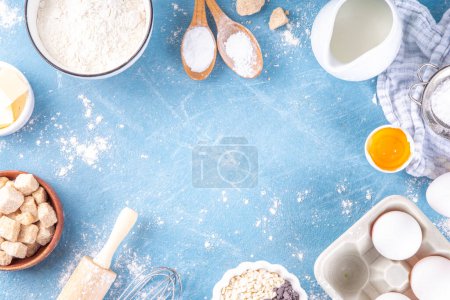 Baking ingredients background. Cooking ingredients (flour, eggs, milk, brown sugar, butter) with utensils on light blue background top view copy space