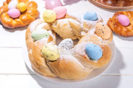Easter wreath bread, traditional Easter holiday baking, sweet bun cakes with colorful Easter eggs, on brunch holiday decorated table copy space