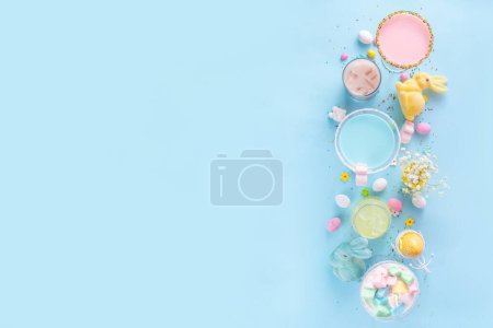 Téléchargez les photos : Moquettes de fête de Pâques colorées pastel pour enfants, boissons non alcoolisées crémeuses et glacées avec barbe à papa, guimauve, pépites de sucre et œufs de Pâques, sur fond bleu rose pastel espace de copie - en image libre de droit