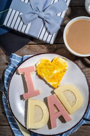 Photo for Father day breakfast sandwiches and scrambled eggs.Homemade father day bacon cheese toasts sandwiches with lettering I love dad, with coffee latte cup, gift box and necktie top view copy space - Royalty Free Image