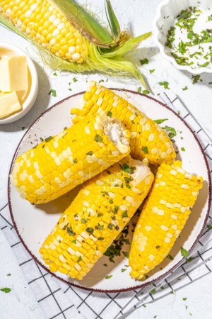 Foto de Boiled corn with butter and herbs. Ripe yellow organic cooked corn cobs, on a white kitchen table - Imagen libre de derechos