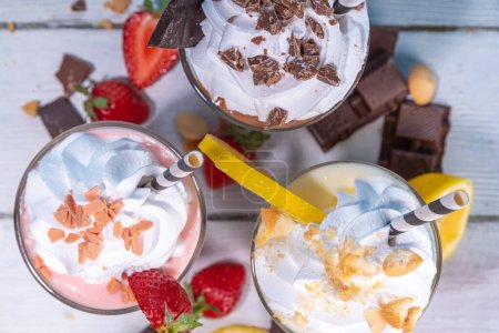 Set of summer refreshing milkshakes or smoothies with classic delicious taste - vanilla lemon, strawberry, chocolate, with whipped cream and toppings, On a white wooden light blue sunny background 