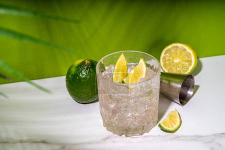 Téléchargez les photos : Cocktail froid à base d'alcool de punch Ti glacé, petit punch, boisson mélangée à base de rhum avec garniture de tranches de lime fraîche, sur fond vert de haute couleur - en image libre de droit