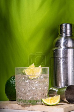 Téléchargez les photos : Cocktail froid à base d'alcool de punch Ti glacé, petit punch, boisson mélangée à base de rhum avec garniture de tranches de lime fraîche, sur fond vert de haute couleur - en image libre de droit