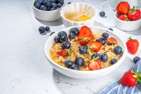 Photo for Summer morning oatmeal with berry. Homemade healthy breakfast oats with strawberry, blueberry, honey, nuts and mint on white marble background - Royalty Free Image