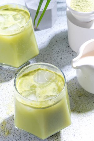 Téléchargez les photos : Thé vert matcha froid. Cocktail de latte matcha glacé dans deux verres avec feuilles de palmier tropical d'été sur fond blanc - en image libre de droit
