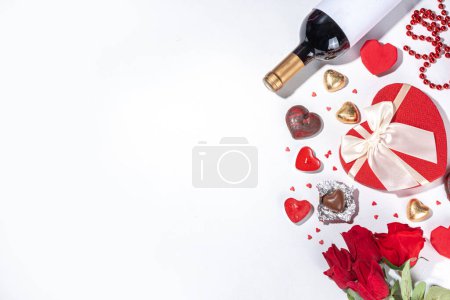 Foto de Valentine's Day greeting card flat lay. Valentine day isolated white background with wine bottle, heart sweets chocolates, bouquet of red roses, gift box, heart shaped candies, confetti, beads - Imagen libre de derechos