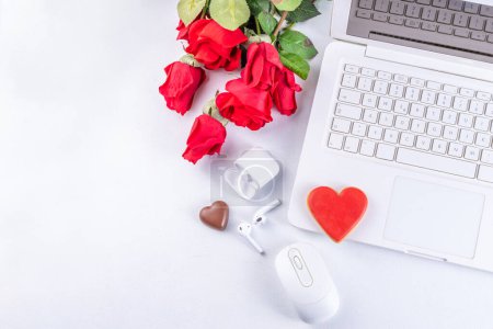 Foto de Woman using laptop with red roses. White laptop on white table background with chocolates, cookie hearts, red roses bouquet, flat lay working holiday, Valentine day background, top view copy space - Imagen libre de derechos