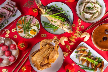 Photo for Traditional Chinese lunar New Year dinner table, party invitation, menu background with pork, fried fish, chicken, rice balls, dumplings, fortune cookie, nian gao cake, noodles, chinese decorations - Royalty Free Image