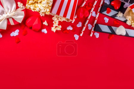 Romantisches Datum am Valentinstag, 14. Februar. Liebesfilm-Marathon, Date im Kino. Klappbrett, Popcorn-Eimer, Herzdekor und Pralinen auf rotem Hintergrund