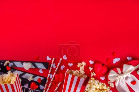 Romantisches Datum am Valentinstag, 14. Februar. Liebesfilm-Marathon, Date im Kino. Klappbrett, Popcorn-Eimer, Herzdekor und Pralinen auf rotem Hintergrund