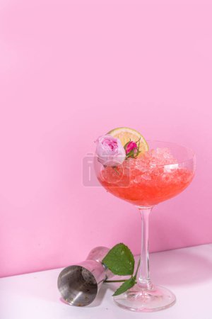 Téléchargez les photos : Cocktail de daiquiri ou margarita de rose congelé, champagne, alcool de vin de rose rose avec des fleurs de roses et des tranches de citron vert - en image libre de droit