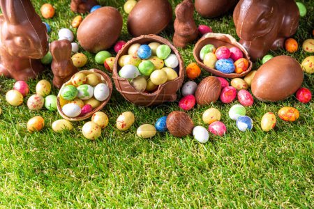 Fondo de caza de huevos de Pascua. Varios dulces y chocolates Huevos de Pascua, conejitos y conejos con canasta para huevos sobre hierba verde parque o fondo de jardín