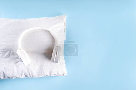 Sonic Hues and Noise for sleep concept mit bequemen Kopfhörern und weißem Kissen auf hellblauem Hintergrund von oben Kopierraum
