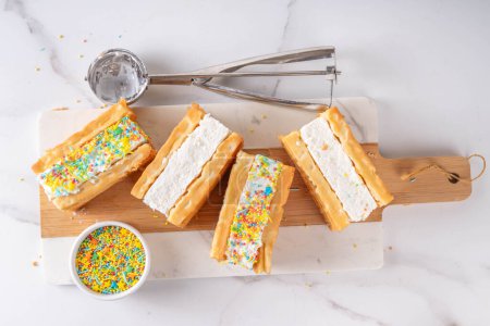 Téléchargez les photos : Sandwichs à la crème glacée gaufrée. Crème glacée savoureuse aux gaufres belges moelleuses et saupoudrées de sucre, délicieux dessert d'été, sur fond blanc avec cuillère à crème glacée - en image libre de droit