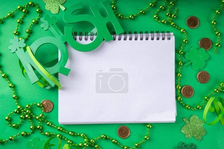Photo for Shamrock saint patrick's day background, St. Patrick's holiday flat lay with party accessories, decor, and blank notepad for your text on green background - Royalty Free Image