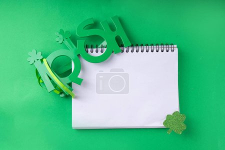 Photo for Shamrock saint patrick's day background, St. Patrick's holiday flat lay with party accessories, decor, and blank notepad for your text on green background - Royalty Free Image