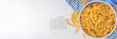 Pasta de Mafaldina cruda sin cocer con ingredientes para cocinar. Pasta italiana corta de Mafaldine con aceite de oliva, tomates cherry, albahaca, especias en la mesa de la cocina blanca, espacio de copia de fondo