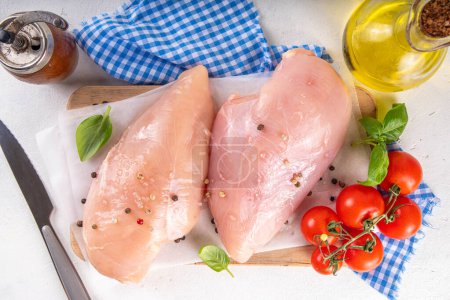 Raw uncooked chicken breast fillet on kitchen table with spices. White lean meat cooking background, white table copy space