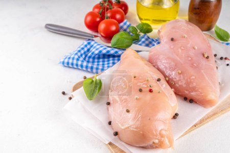 Raw uncooked chicken breast fillet on kitchen table with spices. White lean meat cooking background, white table copy space