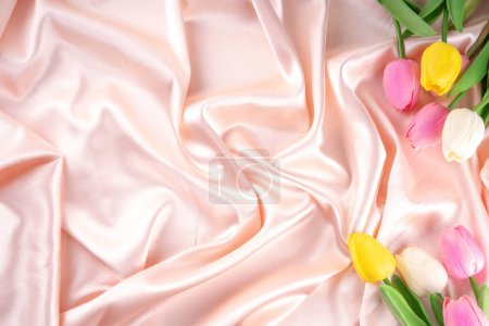Photo for Simple beautiful tulip flower bouquet on satin fabric background. Gently pink pearl cream waves folded satin fabric, with shimmers of light, the surface, flat lay mockup copy space for product or text - Royalty Free Image