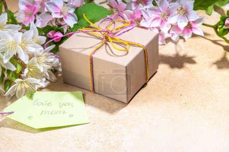 Mother day greeting card background with present and flowers. Gift box with festive ribbon, tag Love you mom, spring bloom flowering branches bouquet flatlay copy space