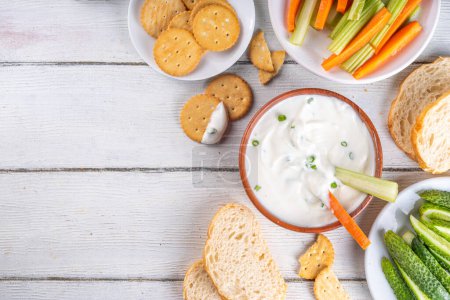 Cottage cheese high-protein dip with fresh vegetables, bread and crackers on wooden white table copy space. Eating diet healthy curd cheese spread with various snacks