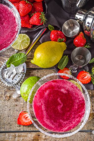 Kalter Alkohol im Sommer. Erdbeer-Margarita-Cocktail mit Limette, Minze und frischer Erdbeere auf rustikalem Holzgrund