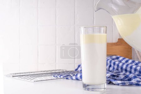 Leche no homogeneizada, leche entera, productos lácteos en capas de crema, concepto Creamline Milk. Granja ecológica natural, leche no pasteurizada en vaso y jarra, en espacio de copia de mesa de cocina blanca