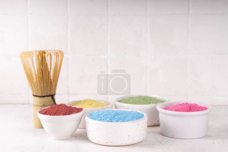 Set getrockneter pflanzlicher Matcha-Pulver in einer weißen Schüssel. Verschiedene Farben und Extrakte Matcha - grün, gelb, rosa, rot, zur Herstellung fruchtiger gesunder Matcha-Teegetränke auf weißem Hintergrund Kopierfläche