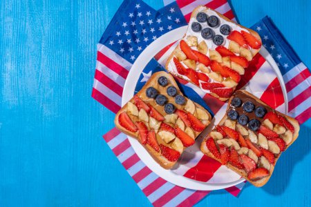  July 4 breakfast sandwiches, holiday snack or brunch with peanut butter, chocolate and cheese spread, with strawberries, blueberries and banana in the shape of america patriotic flag