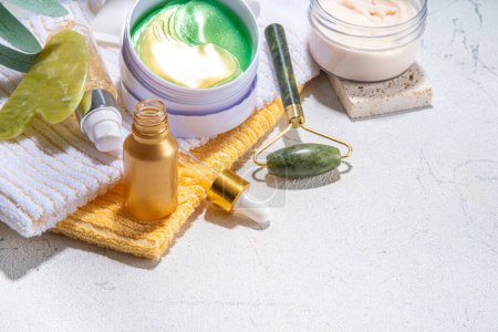 Nature anti-aging cosmetics, therapy massage. Asian beauty skin care. Jade roller, gua sha massager with various organic serum, gel, herbal extract, spa towels. Flatlay on white marble background