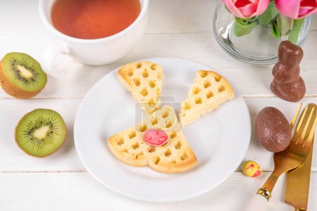 Easter breakfast or brunch. Cute creative decorated soft sweet belgian waffles shaped in form of Easter bunny rabbit, with chocolate eggs and fruits