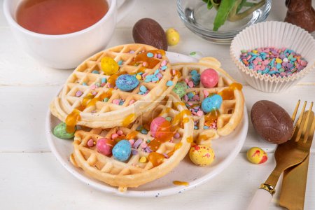 Easter breakfast or brunch. Cute creative decor portion of soft sweet belgian waffles with Easter chocolate eggs, sugar sprinkles and jam or syrup drizzles