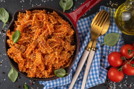 Mafaldine pasta with tomato sauce, italian bolognese, tomato marinara, vegan mushroom or eggplant sauce pasta on black concrete background, with ingredients and spices, copy space