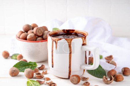 Homemade Hazelnut hot chocolate in a white mug, with a lot of hazelnuts on white wooden background, copy space