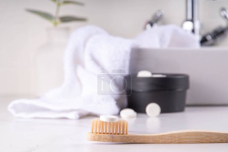 Téléchargez les photos : Pilules dentifrice comprimés sur brosse à dents, comprimé de dentifrice solide blanc avec brosse à dents en bambou sur fond de salle de bain moderne blanc - en image libre de droit