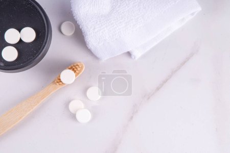 Toothpaste pills tablets on toothbrush, white solid toothpaste tablet with bamboo toothbrush on modern white bathroom background